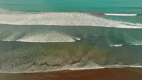 Aerial view of long ocean waves rolling toward the sandy shore in Costa Rica