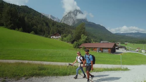 Interracial hiking couple walks by with green valley and mountain peak in background midday