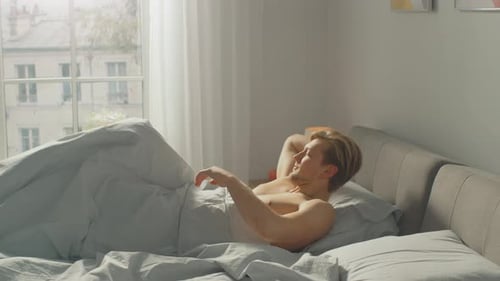 Young man waking up and stretching in bed