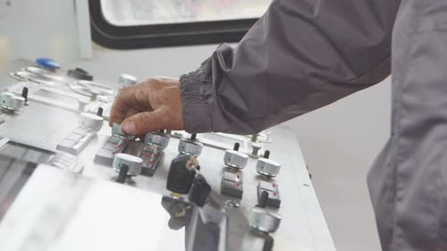 La mano del empleado gira las palancas redondas en el panel de control