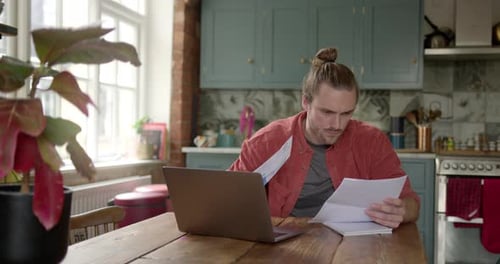 Hombre adulto joven en casa pagando cuentas, financiación de la vivienda en una computadora portátil en la cocina