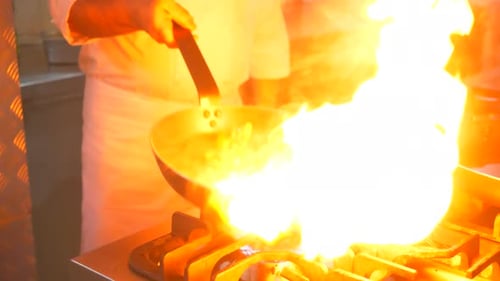 Ein Koch in der Küche kocht und mischt Paprika mit einer großen Flamme, Nahaufnahme