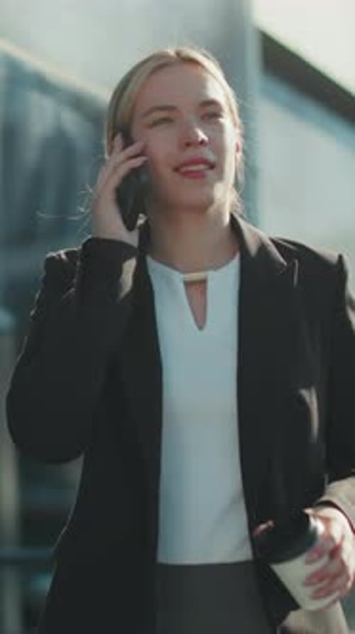 Professional Woman Smiling on Phone Call with Coffee in Hand Near Glass Building
