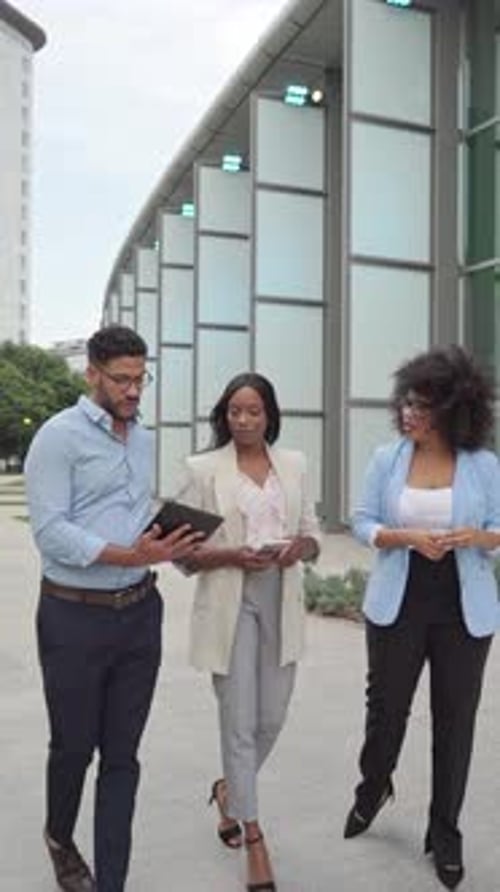 Vertical video of group of multiracial business colleagues walking outdoors with tablet