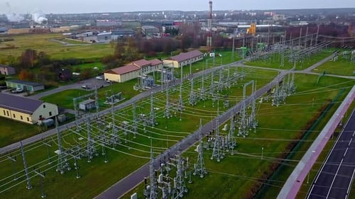 Aerial drone rotating shot over a high voltage power distribution substation on a cloudy day.
