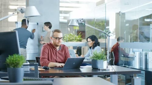 Busy International Corporate Office, Caucasian Man Working at His Desk on a Laptop. In Background C