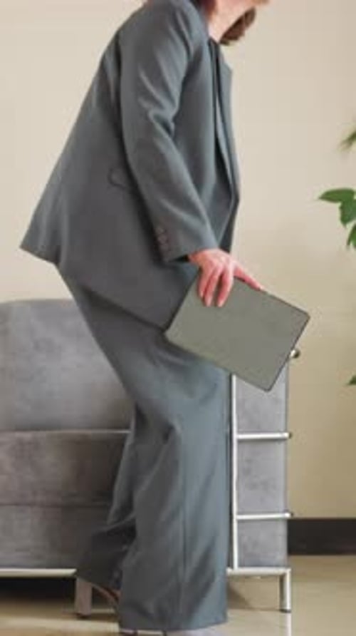 Business Professional In Gray Suit Walking Through Modern Office Lobby With Notebook