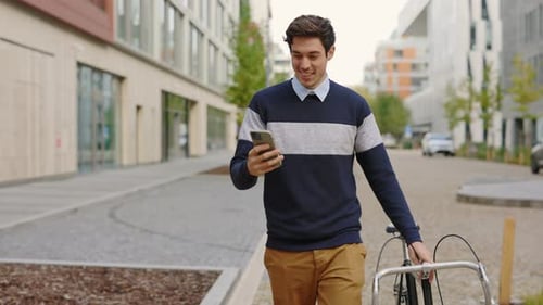 Young Man Walking Bike and Looking at Phone