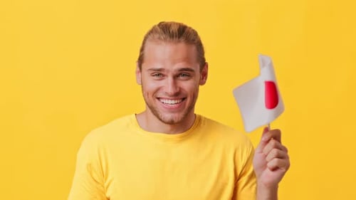 Fröhlicher junger Mann schwenkt japanische Flagge vor hellgelbem Hintergrund