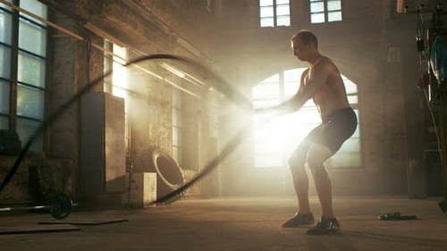 Strong Muscular Shirtless Sportsman Works out Hard with Battle Ropes as Part of His Cross Fitness T
