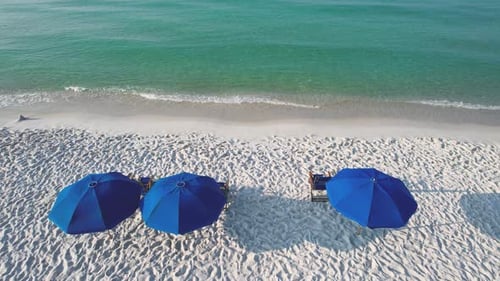 aerial view of blue umbrellas on white sand beach beach on the clear waters of the Gulf of Mexico on