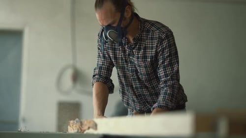 Carpenter in a Respirator Mask Sawing Wood Plank