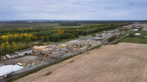 Territory of asphalt plant with building materials beside to agricultural field