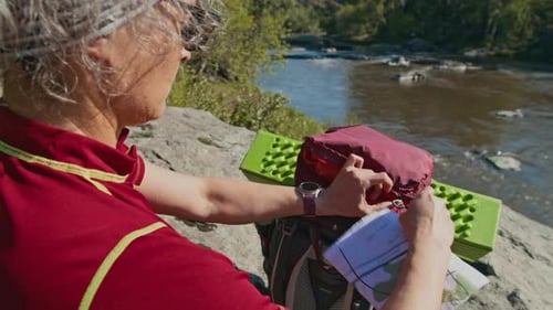 Woman Looks at Map Near River Rocks