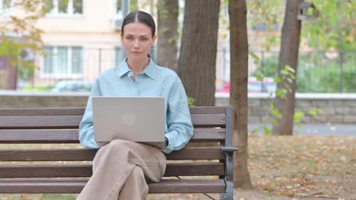 Woman Using Laptop on Park Bench in City