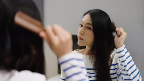 stressed woman suffering hair loss problem with her hairbrush in mirror at home