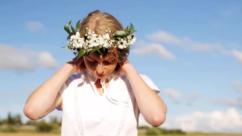 Joven sonriente en una corona de flores silvestres disfruta del sol de verano al aire libre