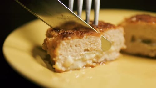Cortar chuletas de pollo Cordon Bleu con queso en el interior con cuchillo y tenedor