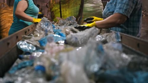 Workers in special wear sorting plastic garbage on a conveyor belt at waste recycling factory