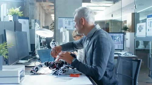 Computer Engineer Walks Into Robotics Branch Room, Talks With Specialists Working on a Robot Design