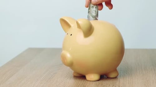 Frau zahlt vorsichtig Geld in ein keramisches Sparschwein auf einer Holzoberfläche ein, um zukünftige Fonds zu finanzieren