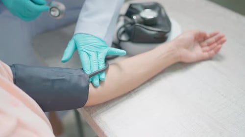 Female nurse wearing a uniform is measuring a patient's blood pressure in a private hospital room