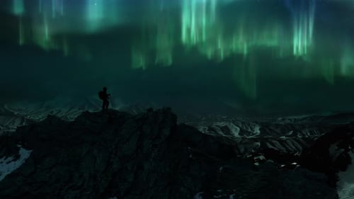 Man on Icy Rock Summit of Snowy Mountain Panorama Watching Polar Lights Aurora Borealis