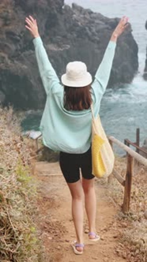 Carefree Woman Exploring Cliffside on Vacation with Arms Raised