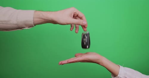 Male Hand Gives a Car Keys to Famale Hand on the Green Background
