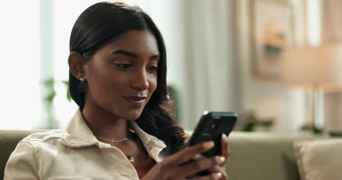 Indian woman, phone and scroll on sofa at home, reading and typing on mobile application in lounge