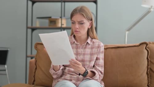 Upset Young Woman Shocked while Reading Documents at home