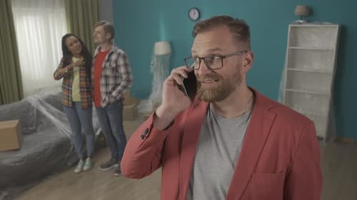 Realtor with a Phone Near His Ear Close Up While a Young Couple is Inspecting a New Apartment a