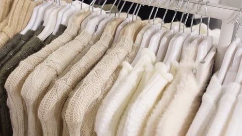 A Collection of Neutral Colored Knitted Sweaters Hanging on Display Rack in a Fashion Store