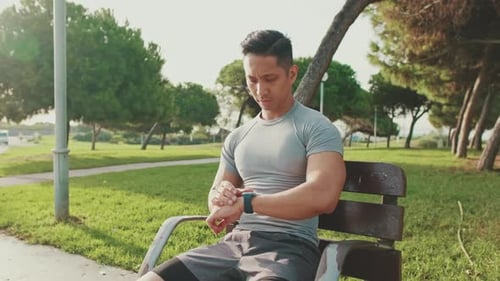Young man sitting on a park bench using smart watch