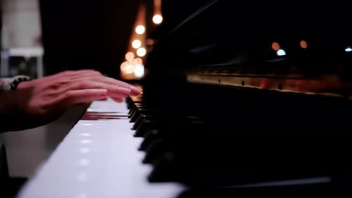 Close up of a woman's hands playing the piano with blurry lights on the background