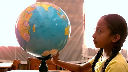 Little girl looking at globe in classroom