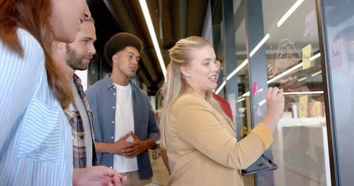 Felizes, diversos colegas criativos discutindo ideias, fazendo anotações em parede de vidro, câmera lenta