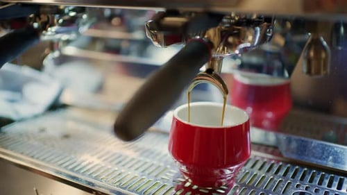Close up of fresh espresso pouring from a commercial espresso machine into a small red ceramic cup