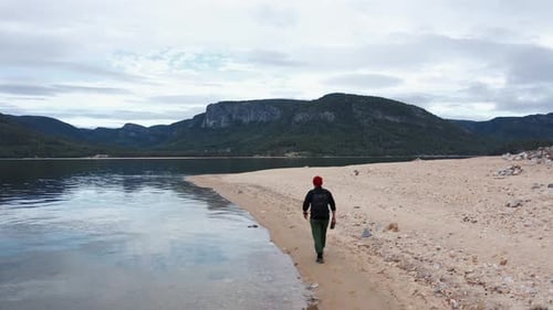 Guy Traveler geht mit einem Rucksack am Ufer entlang eines schönen Sees