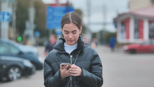 A Girl Walks Through Town and Looks Through Her Phone