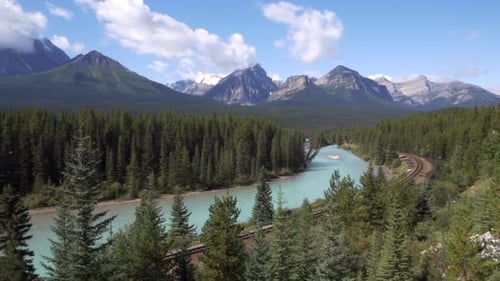 Türkisfarbener Fluss in einer atemberaubenden Landschaft, Berge im Hintergrund und Bahngleise im Hintergrund