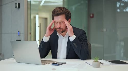Stressed Businessman Experiences Headache at Office Desk