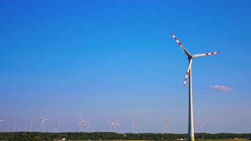 Tall wind turbine rotating in the blue clear sky. Wind farm in the fields at backdrop.