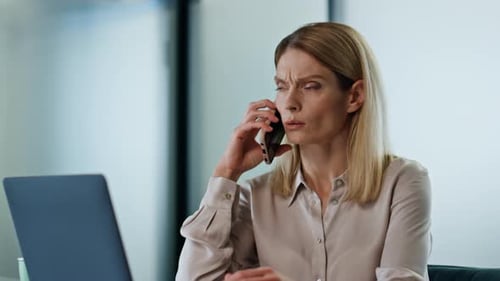 Woman talking on phone at desk using laptop