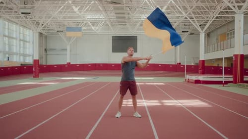 Man Athlete Waves Large Ukrainian Flag at Indoor Stadium