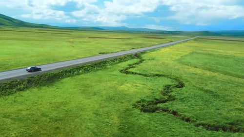 Shooting from drone shows highway among mountains of meadows. Car rushes