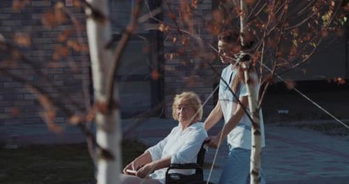 Woman Pushes Senior Woman in Wheelchair Outdoors