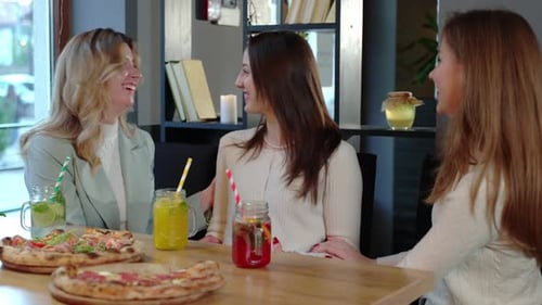 Lächelnde junge Freundinnen, die Pizza und Getränke im Restaurant essen