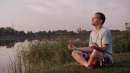Young Adult Meditating on Lakeside at Sunset