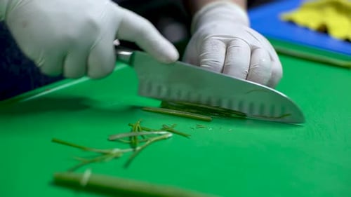 Chef hands cutting green onion on green cutting board, close up. Cutting green onion into slice with